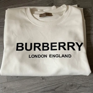 Vit hoodie från Burberry - Vit sweatshirt från Burberry med svart logotyptryck på bröstet. Klassisk rund halsringning, Den kanske har någon fläck på armen men man kan enkelt ta bort den. Den är köpt på plick och den passade tyvärr inte mig.  ribbade muddar och avslut. Mjuk och skön bomullskänsla, perfekt för en clean och stilren look.  Storlek S. En galet snygg hoodie för dig som vill ha något till bra pris, hör av dig vid minsta fundering. Pris är ej hugget i sten 🪨 