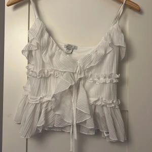 Vit volangig linnetopp från Missu/newyorker💗 - Supersöt vit linnetopp från Missu med tunna axelband, volanger och knyt framtill. Toppen har ett lätt ribbat tyg och flera lager volanger som ger en romantisk vibe. Perfekt för varma dagar när du vill känna dig extra fin. Oanvänd