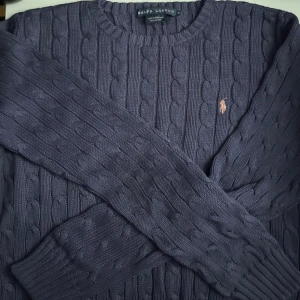 Mörkblå kabelstickad tröja Ralph Lauren - Barn storlek tror jag för den är väldigt liten,   Kabelstickad mörkblå tröja från Ralph Lauren i 100% bomull. Klassisk rund halsringning och broderad logga i beige på bröstet. Perfekt för lager-på-lager och snygg till jeans eller kjol. Långärmad och riktigt skön att bära. Skriv om du är intresserad eller vill ha mer bilder