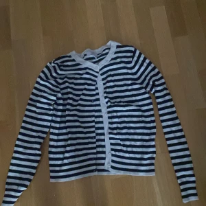 Randig kofta från H&M, svart och vit - Snygg randig kofta från H&M i svart och vitt. Koftan har långa ärmar, knappar framtill och är tillverkad i mjuk bomull. Perfekt för lager-på-lager och enkel att matcha med jeans eller kjol.