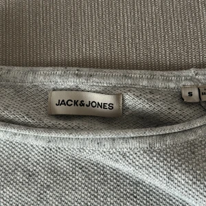 Ljusgrå stickad tröja Jack & Jones - En stilren ljusgrå stickad tröja från Jack & Jones i storlek S. Tröjan har rund halsringning och långa ärmar, perfekt för lager-på-lager. Enkel design som funkar till det mesta och är riktigt skön att ha på sig.