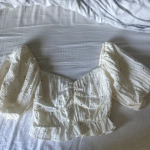 Vit blus med puffärmar och prickar - Supersöt vit blus med svarta små prickar och volangkant nertill. Säljer då den inte kommer till användning aldrig använt heller
