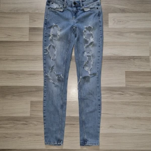 Ljusblå ripped jeans från Gina Tricot  - Säljer ett par ljusblå jeans från Gina Tricot jeans i storlek 26. Jeansen har flera stora slitningar och hål framtill för en riktigt edgy look. De är skinny fit med klassiska fickor och bälteshällor. Perfekta för dig som gillar streetstyle.