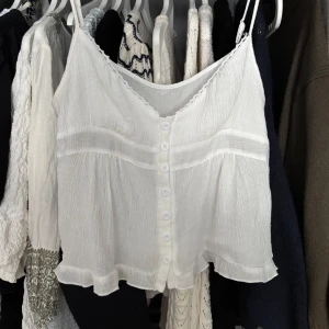 Vit linnetopp  - Supersöt vit linnetopp med smala axelband, knappar framtill och volangkant nertill. Säljer åt min syster som ej har använt den! Köpt från shein storlek M