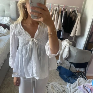 Vit blus med knyt och volang - Supersöt vit blus med smock upptill, knyt framtill och volangiga ärmar. 