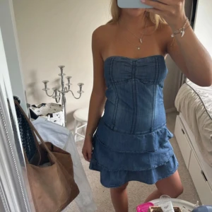 Strapless jeansklänning med volang - Säljer en snygg axelbandslös jeansklänning i blått med volangig kjol. Klänningen är kort och har en fin passform. Jättegullig till sommaren. Pris kan diskuteras 
