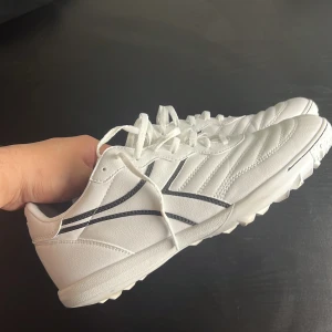 Vita Diadora fotbollsskor strl 41 - Snygga vita fotbollsskor från Diadora med svarta detaljer och klassisk design. Skorna har snörning, mönstrad sula för bra grepp och är tillverkade i syntetmaterial. Perfekta för dig som vill sticka ut på planen med stilrena skor. Använda 1 gång ingen låda kommer med skulle säga att dom är storlek 41 även fast att det står 43 på dom 
