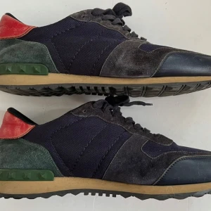 Valentino Rockrunner sneakers i mocka - Snygga Valentino Rockrunner sneakers med svart och mörkblå mesh och mocka, gröna detaljer vid hälen och röd hälkappa. Klassisk gummisula och snörning framtill. Perfekta för dig som vill ha en unik och lyxig sneaker med cool färgkombo.