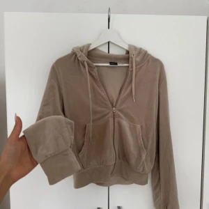 Beige velour hoodie från Gina Tricot - Supermjuk beige hoodie i velour från Gina Tricot. Tröjan har dragkedja framtill, huva med snörning och stora fickor. Långärmad och croppad modell som ger en chill vibe. Perfekt för dig som gillar comfy och trendigt.