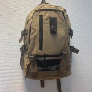 Trendig ryggsäck med svarta detaljer - Snygg ryggsäck med flera fack, svarta dragkedjor och bruna spännen. Praktiska sidofickor i mesh och justerbara remmar. Perfekt för skolan eller utflykten, med coola detaljer som svart knappstängning framtill. Rymmer allt du behöver till vardagen. Ny 