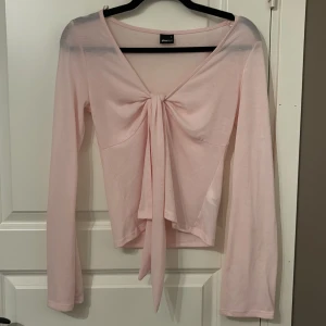 Ljusrosa långärmad knytblus - Supersöt ljusrosa långärmad blus från Gina Tricot med v-ringning och knyt framtill. Tunn och mjuk i materialet, perfekt för lager-på-lager eller som statement-piece. Snyggt croppad passform som ger en trendig look.