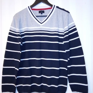 Randig stickad tröja Jack & Jones L - Snygg stickad tröja från Jack & Jones i storlek L. Tröjan är grå och marinblå med vita horisontella ränder, v-ringad hals och långa ärmar. Perfekt för dig som gillar klassisk stil med en modern touch.