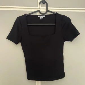 Svart topp från New yorker - Svart, tight topp från Amisu/new yorker med korta ärmar och snygg fyrkantig ringning. Enkel och stilren design som passar perfekt till jeans eller festliga tillfällen! Mjuk och stretchig känsla i materialet för en bekväm passform.