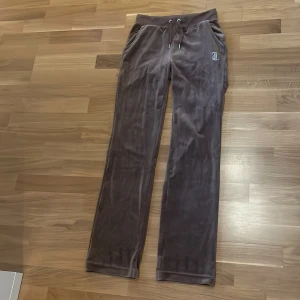 Bruna velourbyxor Juicy Couture XS - Mysiga bruna mjukisbyxor från Juicy Couture i velour med snörning i midjan och fickor fram. Stenprydd Juicy-logga på baksidan och liten logga fram. Perfekta för en chill och trendig look. Endast använda ett fåtal gånger 