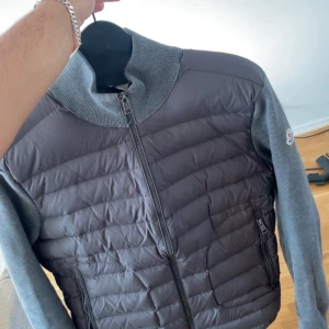 Grå Moncler pufferjacka med stickade ärmar - Säljer min fina moncler Cardigen jacka som jag har fått i present och den va lite liten på mig och därför vill jag sälja den, jag har tyvärr inget kvitto på den, priset kan alltid diskuteras vid en snabbaffär☺️