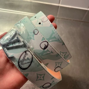  mintgrönt bälte - Snyggt bälte från  i mintgrönt och vitt med ikoniskt -mönster och silverfärgat spänne. Bältet har en bred design och är tillverkat i skinn med tryckt logotyp och detaljer i svart. Perfekt för att lyfta din outfit med en lyxig touch.