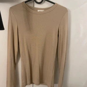 Beige ribbad långärmad tröja Gina Tricot - En basic beige långärmad tröja från Gina Tricot, Basically Basics-kollektionen. Tröjan är ribbad och har en rund halsringning. Perfekt att styla med jeans eller kjol för en clean look.