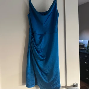 Blå satin klänning med drapering - Supersnygg blå klänning i satin med smala axelband och draperad detalj på sidan. Modellen är figurnära och har en stilren, enkel look som ändå sticker ut tack vare färgen och materialet. Perfekt för dig som vill ha något trendigt och elegant. Den går till mitten utav låren💕💕 aldrig använt! Skriv vid frågor💕