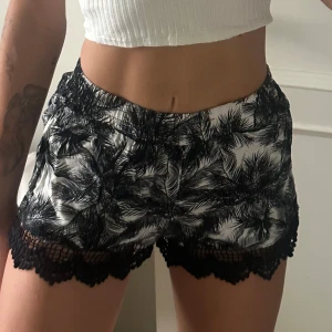 Shorts med palmer och spets - Snygga shorts i svartvitt palmbladsmönster med med sexig spetskant nertill. Lätta och luftiga. Aldrig används. Frakt ingår i priset