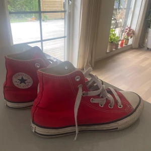 Röda Converse All Star high-tops - Klassiska röda Converse All Star high-tops med vit tå och sula, vita snören och silverfärgade öljetter. Skorna är i textil med gummisula och har den ikoniska loggan på sidan. Perfekta för en cool och avslappnad stil.