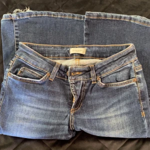 Lowwaist jeans från Hunkydory - Snygga mörkblå jeans från Hunkydory med klassisk femficksdesign och kontrastsömmar. Jeansen har en något tvättad look och råa kanter nertill för en cool vibe. Tillverkade i mjukt denimtyg som sitter skönt hela dagen. 
