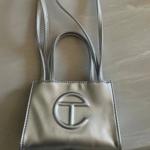 Silver mini handväska från Telfar - Säljer en mini handväska från Telfar i metallic silver. Väskan har både korta handtag och långa axelband, samt Telfars logga på framsidan. Har använt den en gång och kommer som ny🩷