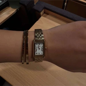 Guldfärgad rektangulär klocka - Elegant guldfärgad klocka med rektangulär urtavla och romerska siffror. Armbandet är i metall med en klassisk länkdesign. Perfekt för en stilren look.