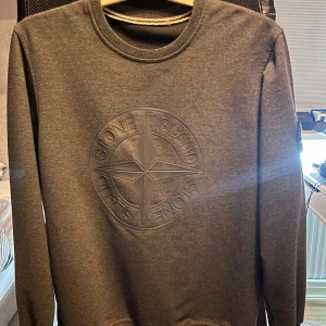 Svart sweatshirt från Stone Island - Säljer en stilren grå sweatshirt från Stone Island med deras ikoniska kompassmärke broderat på bröstet. Tröjan har långa ärmar och en rund halsringning. Perfekt för en avslappnad och trendig look.