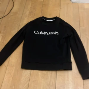 Svart tröja från Calvin Klein - Säljer en stilren svart tröja från Calvin Klein med deras ikoniska logga tryckt på framsidan. Tröjan har långa ärmar och en rund halsringning. Perfekt för en avslappnad och trendig look.