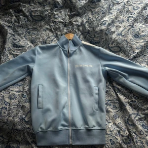 Ljusblå track jacket från Palm Angels - Säljer min fräscha Palm Angels tröja, inte använd mer än 5-6 gånger, säljes då den inte passar längre. Skicket är 9/10