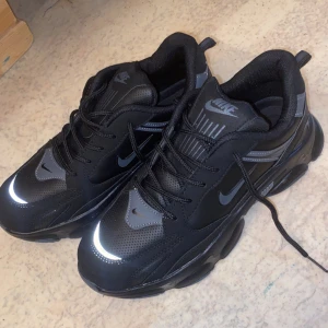 Svarta sneakers från Nike - Snygga svarta sneakers från Nike med reflekterande detaljer och snörning. Perfekta för en sportig look med en robust sula för extra komfort. Tillverkade i syntetmaterial för hållbarhet och stil.