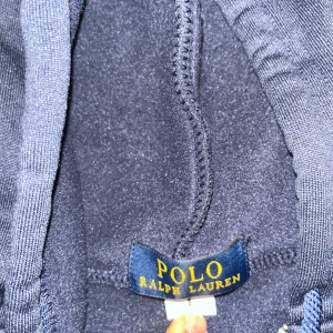 Mörkblå hoodie från Polo Ralph Lauren - Säljer en snygg mörkblå hoodie från Polo Ralph Lauren med dragkedja och huva. Den har en liten röd broderad logga på bröstet och snören vid huvan. Perfekt för en casual look!