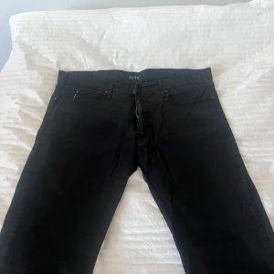 Svarta jeans från Armani - Snygga svarta jeans från Armani med klassisk femficksdesign och diskret logga på bakfickan. Perfekta för en stilren look. De har en dragkedja och knapp framtill. Aldrig använd. Mycket bra skick