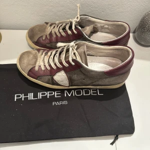 Sneakers från Philippe Model - Snygga sneakers från Philippe Model i en kombination av beige och vinrött. Skorna är använda och relativt slitna framförallt i både sulorna, som kan ses på bild 4! Box medkommer vid köp! Storlek 41-42