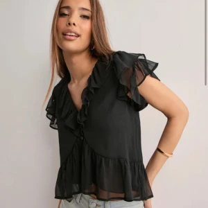Svart blus med volangdetaljer - Snygg svart blus med volangdetaljer och korta ärmar från NELLY,  nypris 299kr💞Aldrig använd