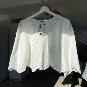 Vit blus med spetsdetaljer - Säljer en vacker vit blus i linneblandning med spetsdetaljer vid halsen och nederkanten. Blusen har långa ärmar och en knytning i nacken. Perfekt för en somrig look! Det står L, men passar mig som brukar ha XS-S