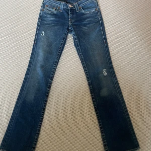 Blå jeans från True Religion - Snygga blå jeans från True Religion med slitna detaljer och klassisk femficksdesign. Midja 38cm och innerbensmåttet 83cm. Jag är 171 och de är bra i längden på mig