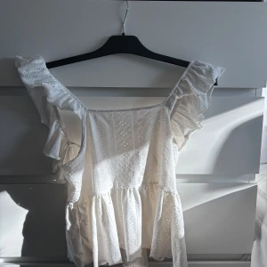 Vit blus med volangdetaljer - Charmig vit blus med volangdetaljer och spetsmönster. Blusen har en luftig passform och knytning i ryggen, perfekt för varma sommardagar. Hör av dig vid intresse 🤗