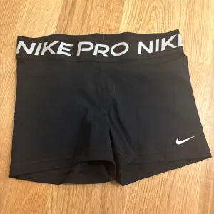 Svarta träningsshorts från Nike - Säljer ett par svarta Nike Pro träningsshorts med elastisk midja och vit logga. Perfekta för intensiva träningspass eller löpning. De är tillverkade i ett stretchigt material för optimal rörelsefrihet.