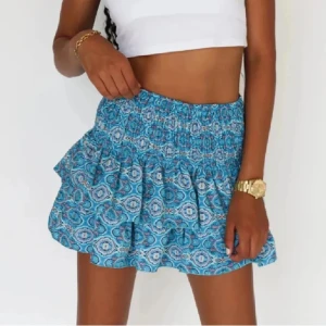 Blå mönstrad kortkjol - Snygg blå kortkjol med ett unikt mönster och volangdetaljer. Perfekt för en somrig look. Kjolen har en elastisk midja för en bekväm passform.