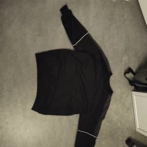 Svart långärmad tröja med vita detaljer - Säljer en svart långärmad tröja med vita detaljer längs ärmarna. Perfekt för en stilren och enkel look. Tröjan har en normal passform och är tillverkad i ett mjukt material.