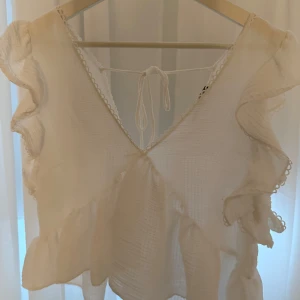 Vit blus med volanger - Säljer en söt vit blus med volanger och v-ringning. Blusen har öppen rygg med knytband och är perfekt inför sommaren💕