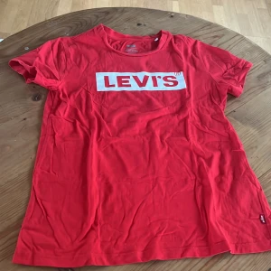 Röd t-shirt från Levi's - Säljer en klassisk röd t-shirt från Levi's med deras ikoniska logga tryckt i vitt på bröstet. T-shirten är kortärmad och perfekt för en avslappnad stil. 