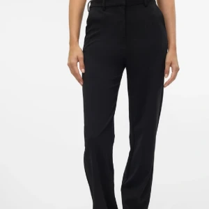 Svarta kostymbyxor från Vero Moda - Snygga svarta kostymbyxor från Vero Moda med hög midja och rak passform. Perfekta för en stilren look. Byxorna har hällor för bälte och en diskret dragkedja framtill.