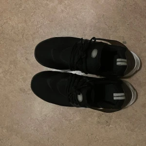 Svarta Nike sneakers - Snygga svarta Nike sneakers med vit sula och snörning. Perfekta för en sportig look. Diskret Nike-logga på sidan och häl. Bekväma och stilrena för vardagsbruk.