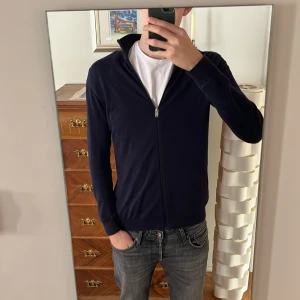 Mörkblå tröja med dragkedja från Selected Homme - Säljer en stilren tunn mörkblå tröja från Selected Homme. Tröjan har en dragkedja framtill och långa ärmar, perfekt för en avslappnad look. Tillverkad i ett mjukt material som ger en bekväm passform. Är 194 cm så passar de flesta som använde L i storlek 