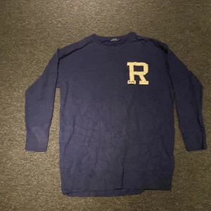Mörkblå långärmad tröja från Polo Ralph Lauren - Säljer en mörkblå långärmad tröja från Polo Ralph Lauren med ett stort vitt 'R' broderat på framsidan. Perfekt för en stilren och avslappnad look. Tröjan är i en klassisk design med rund halsringning.