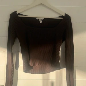 Brun ribbad långärmad topp H&M - Mörkbrun ribbad topp från H&M med lång ärm och bred, fyrkantig urringning. Snygg croppad passform som sitter tajt och markerar midjan. Perfekt att styla med jeans eller kjol för en trendig look.