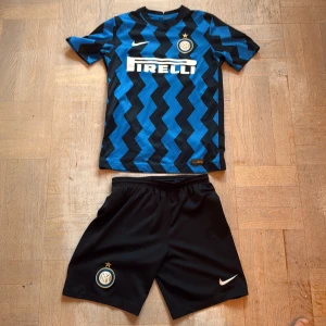 Inter Milan matchställ - Inter Milan matchställ från Nike i storlek L. Tröjan är blå och svart med sicksack-mönster, korta ärmar och Pirelli-logga framtill. Shorts i svart med klubbmärke och Nike-logga. Tillverkat i Dri-FIT-material som andas. Perfekt för fotbollsträning eller support.