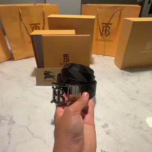 Burberry svart skinnbälte med B-spänne - Säljer ett stilrent svart skinnbälte från Burberry med klassiskt rutigt mönster och ett stort, silverfärgat B-spänne framtill. Bältet kommer med originalförpackning, kvitto och Burberry-kort. Perfekt accessoar för att lyfta din outfit.